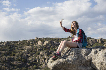 Spanien, Madrid, junge Frau ruht sich auf einem Felsen aus und macht ein Selfie während eines Trekkingtages - ABZF02000