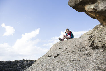 Spanien, Madrid, junge Frau ruht sich auf einem Felsen aus und telefoniert während einer Wanderung - ABZF02003