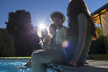 Vier Freunde sitzen am Pool in der Abenddämmerung - ZOCF00303