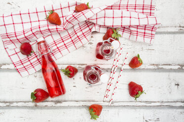 Three glass bottles of homemade strawberry lemonade and strawberries on white wood - LVF06103