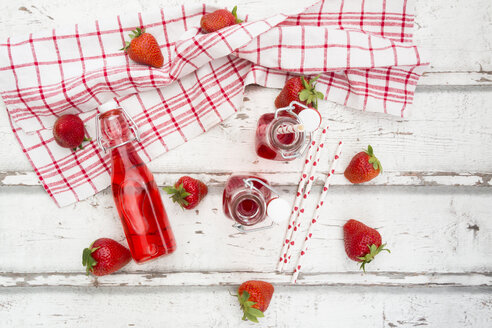 Drei Glasflaschen mit selbstgemachter Erdbeerlimonade und Erdbeeren auf weißem Holz - LVF06103