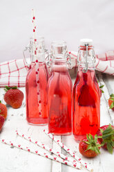 Three glass bottles of homemade strawberry lemonade and strawberries on white wood - LVF06104