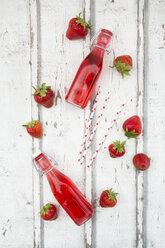 Three glass bottles of homemade strawberry lemonade and strawberries on white wood - LVF06106