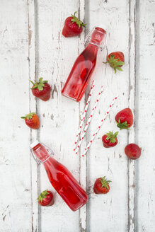 Drei Glasflaschen mit selbstgemachter Erdbeerlimonade und Erdbeeren auf weißem Holz - LVF06106