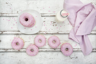 Krapfen mit rosa Zuckerguss und Zuckergranulat und einer Flasche Milch auf Holz - LVF06113