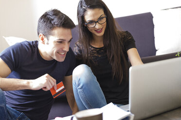 Young couple with credit card using laptop in the living room - FMOF00276