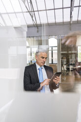 Reifer Geschäftsmann, der im Büro sitzt und ein digitales Tablet benutzt - FMKF04108