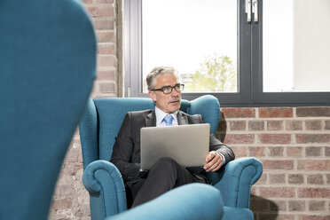 Älterer Geschäftsmann im Sessel sitzend, mit Laptop - FMKF04112