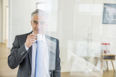 Mature businessman standing in office, drinking coffee - FMKF04114