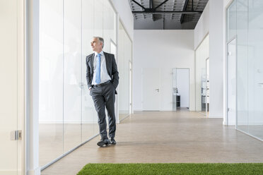 Älterer Geschäftsmann stehend im Büro mit grünem Rasenteppich - FMKF04117