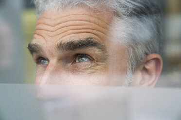 Mature businessman looking through glass pane - FMKF04128