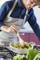 young man preparing broccoli in kitchen - ZOCF00321