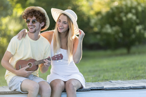 Lachendes junges Paar entspannt sich am Poolrand, lizenzfreies Stockfoto