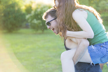 Young man giving his girlfriend a piggyback ride in the garden - ZOCF00350