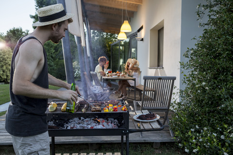 Mann am Barbecue-Grill mit Freunden im Hintergrund, lizenzfreies Stockfoto