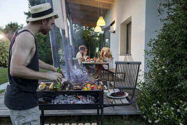 Mann am Barbecue-Grill mit Freunden im Hintergrund - ZOCF00358