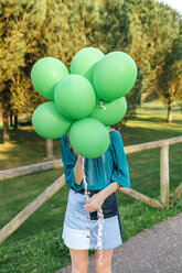 Junge Frau versteckt sich hinter grünen Luftballons - DAPF00755