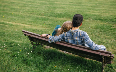 Rückenansicht eines jungen Paares, das auf einer Bank auf einer Wiese sitzt - DAPF00761