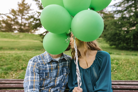 Young couple kissing behind green balloons stock photo