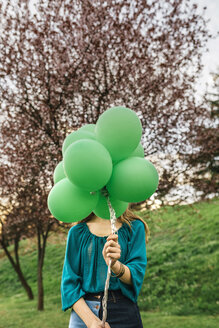 Young woman hiding behind green balloons - DAPF00763