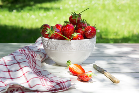 Schale mit Erdbeeren, Messer und Küchenhandtuch auf dem Gartentisch, lizenzfreies Stockfoto