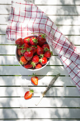 Bowl of strawberries, knife and kitchen towel on garden table - LVF06128