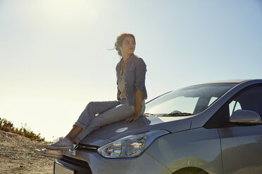 Young woman sitting on a car looking around - SRYF00536