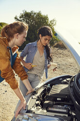 Two young women checking their car standing at the roadside - SRYF00542