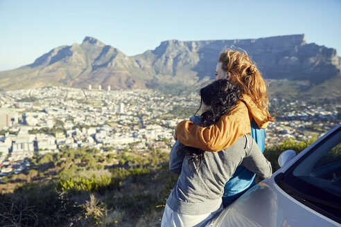 South Africa, Cape Town, Signal Hill, two young women leaning against car overlooking the city - SRYF00548