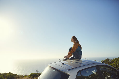 South Africa, Cape Town, Signal Hill, young woman sitting on top of car enjoying the view to the sea - SRYF00551