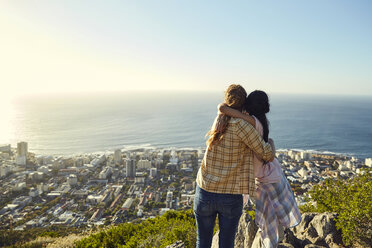 Südafrika, Kapstadt, Signal Hill, zwei junge Frauen umarmen sich mit Blick auf die Stadt und das Meer - SRYF00561