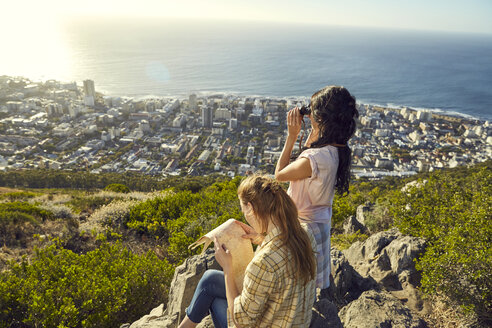 Südafrika, Kapstadt, Signal Hill, zwei junge Frauen mit Karte und Fernglas mit Blick auf die Stadt und das Meer - SRYF00563