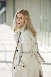 Porträt einer lachenden blonden Frau im Trenchcoat - CHAF01869