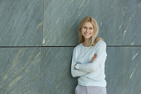 Porträt einer lächelnden blonden Frau, die an der Wand lehnt, lizenzfreies Stockfoto