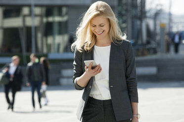 Portrait of smiling blond businesswoman looking at cell phone - CHAF01876