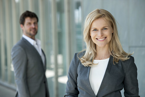 Porträt einer lächelnden Geschäftsfrau mit ihrem Partner, der im Hintergrund zusieht, lizenzfreies Stockfoto