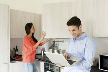 Lächelnder junger Mann mit Frau in der Küche am Laptop - FMOF00280