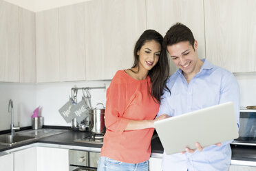 Smiling couple with laptop in kitchen - FMOF00281