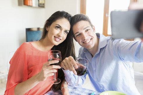 Paar mit Rotweingläsern posiert für ein Selfie - FMOF00284