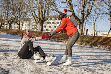Woman helping ice skating friend getting up on canal - MFF03515