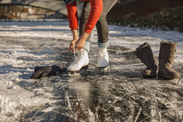 Close-up of woman putting on ice skates on canal - MFF03518