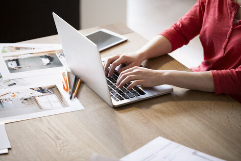 Close-up of woman using laptop surrounded by photographies - FKF02243