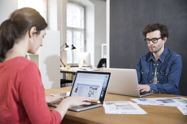 Man and woman using laptops on table in office - FKF02247