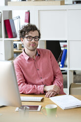 Portrait of confident man sitting at desk in office - FKF02258