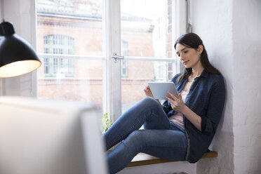 Woman using tablet at the window in office - FKF02274