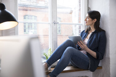 Woman with tablet looking out of window in office - FKF02275