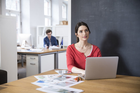 Frau mit Laptop auf Tisch in Büro denken, lizenzfreies Stockfoto