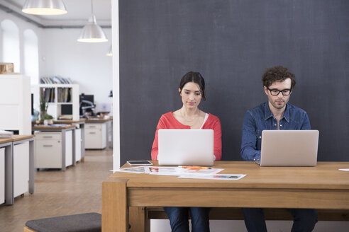 Mann und Frau benutzen Laptops auf einem Tisch im Büro - FKF02282