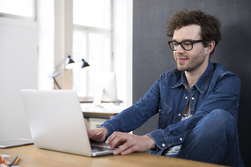 Smiling man using laptop in office - FKF02283