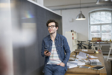 Lächelnder Mann mit Mobiltelefon im Büro - FKF02288